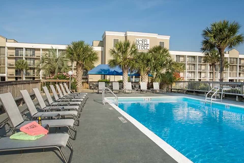 Beachfront hotel pool area with palm trees, blue umbrellas, and multi-story building