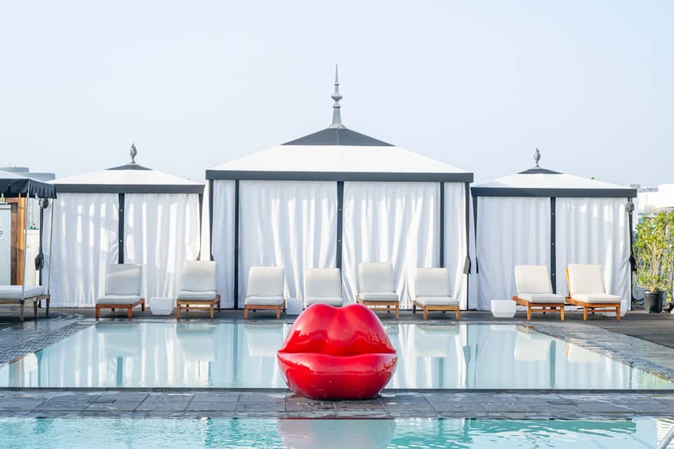 Luxury resort pool area with white cabanas, sheer curtains, and a red sculptural lip float