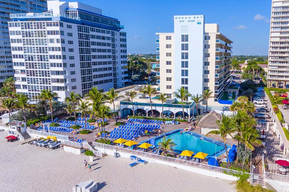 Modern hotel building with Ocean Sky signage, blue loungers, beach, and palm trees