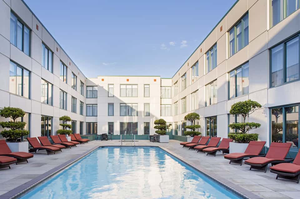 Modern resort courtyard with swimming pool, red lounge chairs, and contemporary white building