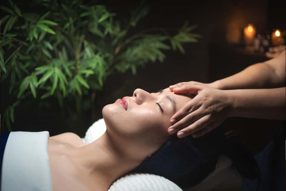 Woman receiving facial massage in spa with ambient lighting and green foliage backdrop