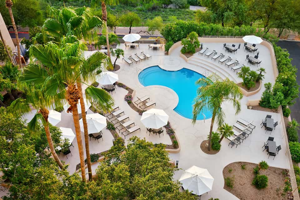 Aerial view of kidney-shaped pool with white umbrellas, lounge chairs, and landscaped grounds