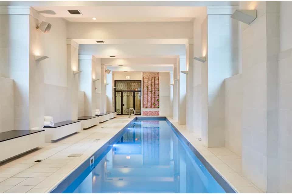Indoor lap pool with white columns, skylights, and decorative panels in modern spa facility