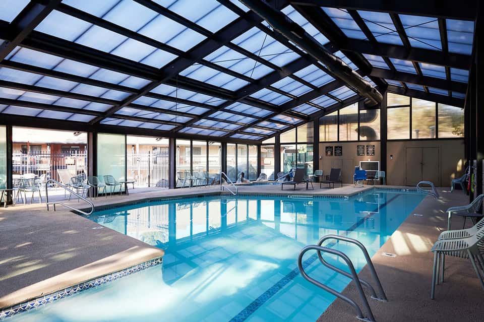 Indoor swimming pool with retractable glass roof, loungers, and large windows overlooking the grounds