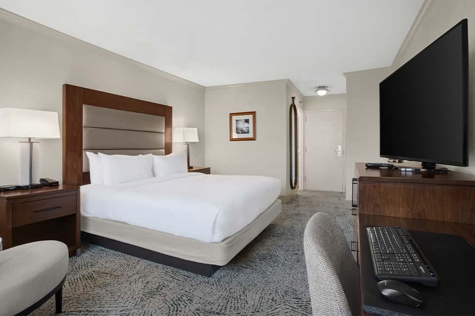 Modern hotel bedroom with king bed, wooden frame, flat-screen TV, and contemporary furnishings