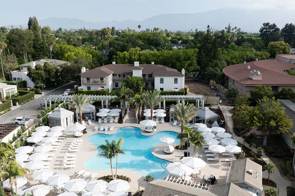 Aerial view of resort with curved swimming pool, lounge chairs, and mountain backdrop