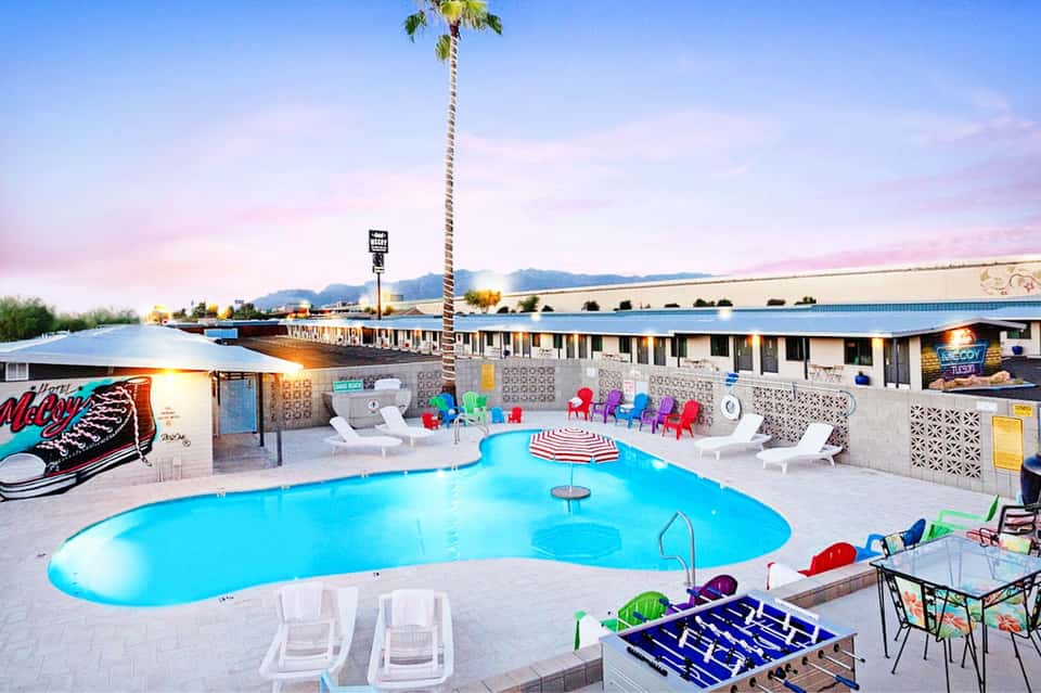 Retro-style motel pool with bright blue water, colorful chairs, and desert mountain view