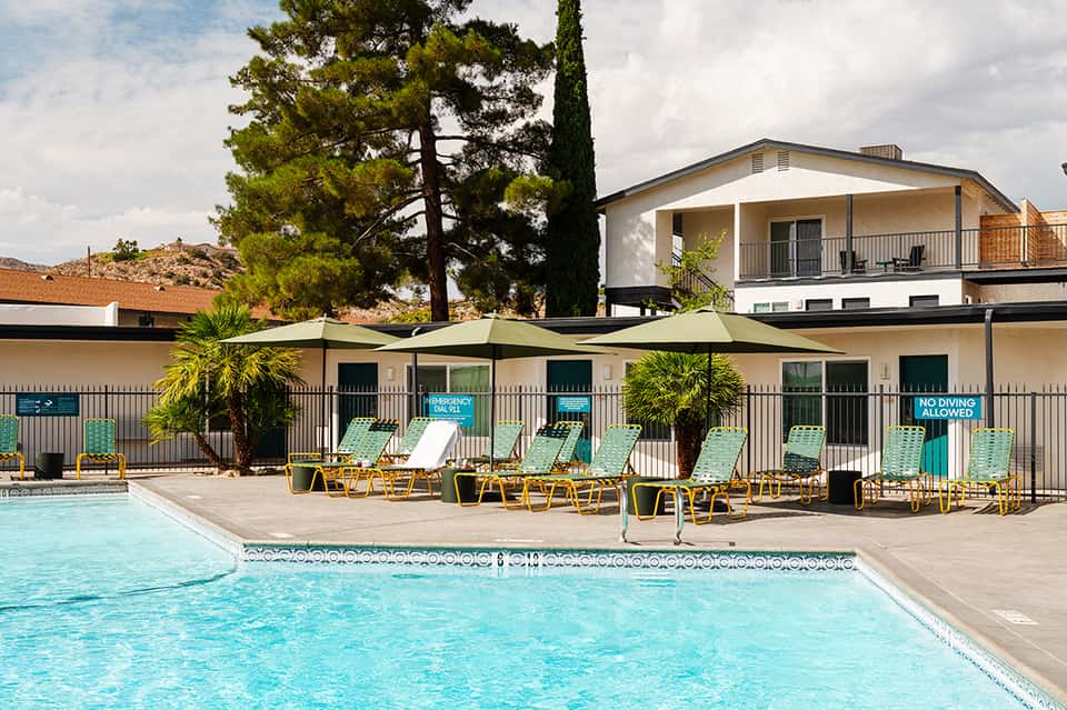 Resort pool with turquoise water, lounge chairs, and shade structures against hillside
