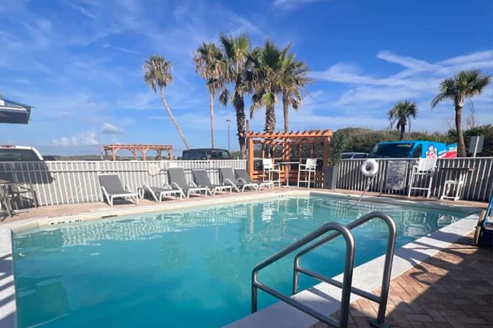 Resort swimming pool with lounge chairs, palm trees, and lake views in background