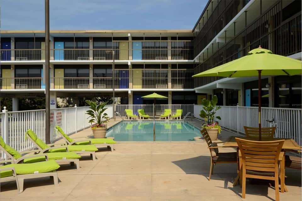 Resort pool area with lime-green lounge chairs, umbrellas, and multi-story building