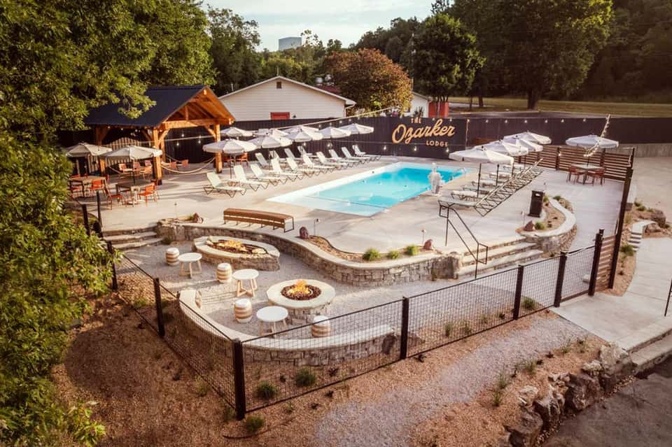 Resort pool area with swimming pool, fire pits, wooden pavilion, lounge chairs, and wooded surroundings