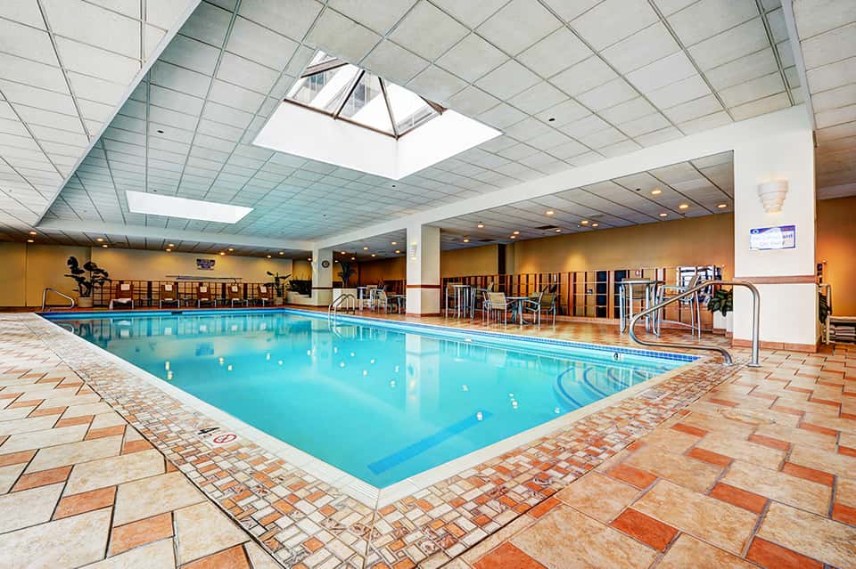 Indoor swimming pool with blue water, seating area, skylights, and orange tiled floor