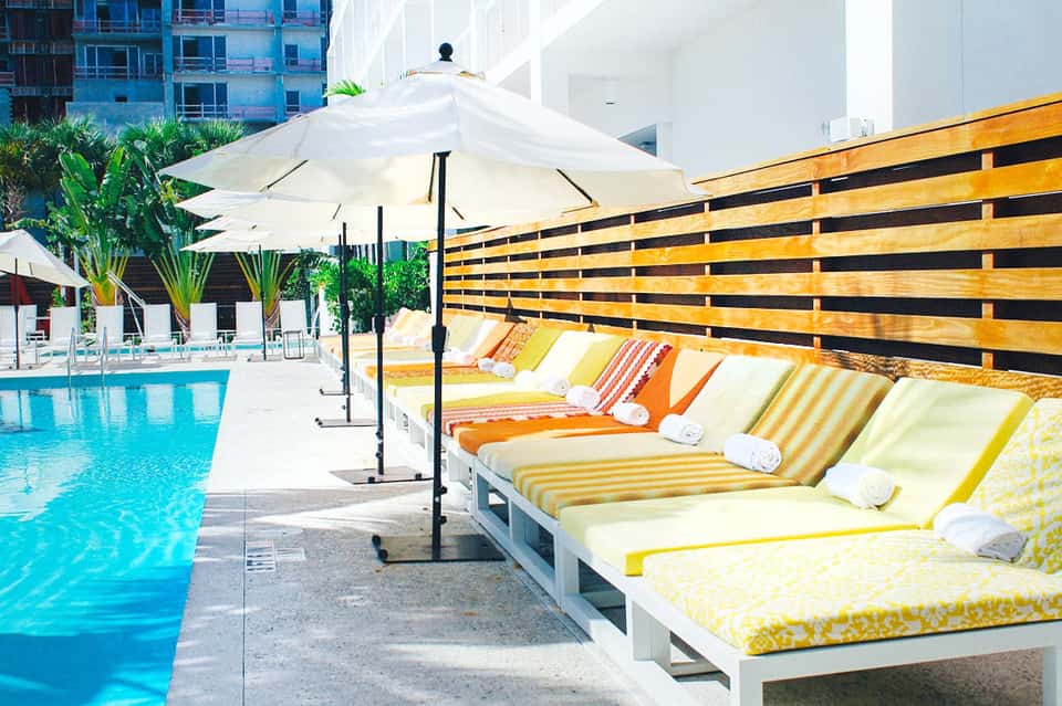 Outdoor pool area with colorful striped lounge chairs, white umbrellas, and wooden privacy fence