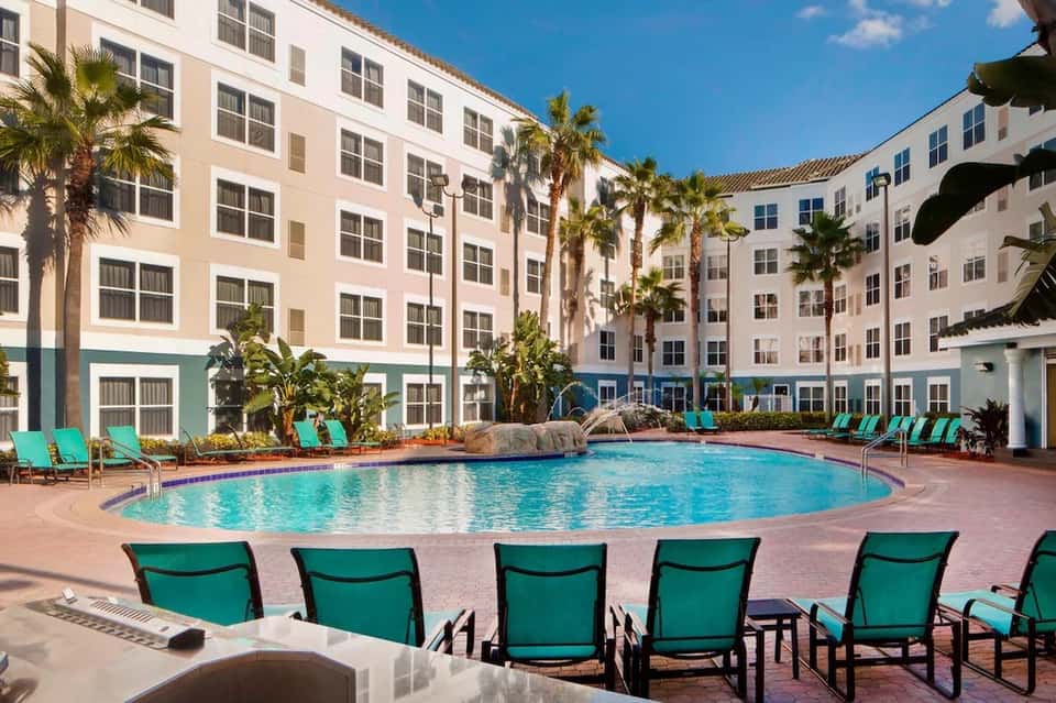Curved resort pool with turquoise water, green lounge chairs, and multi-story building