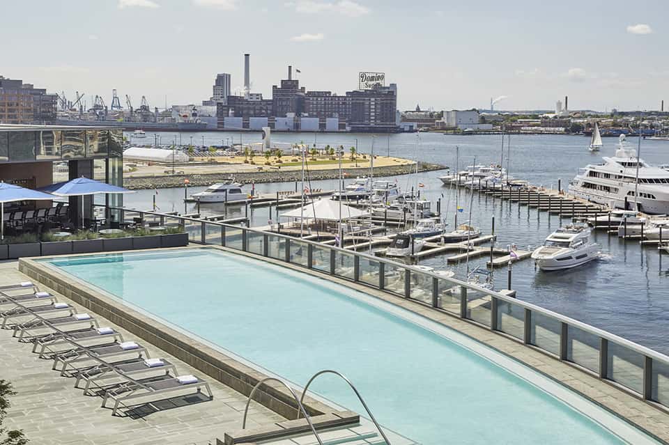 Waterfront hotel pool with marina view, boats docked below, and industrial cityscape backdrop