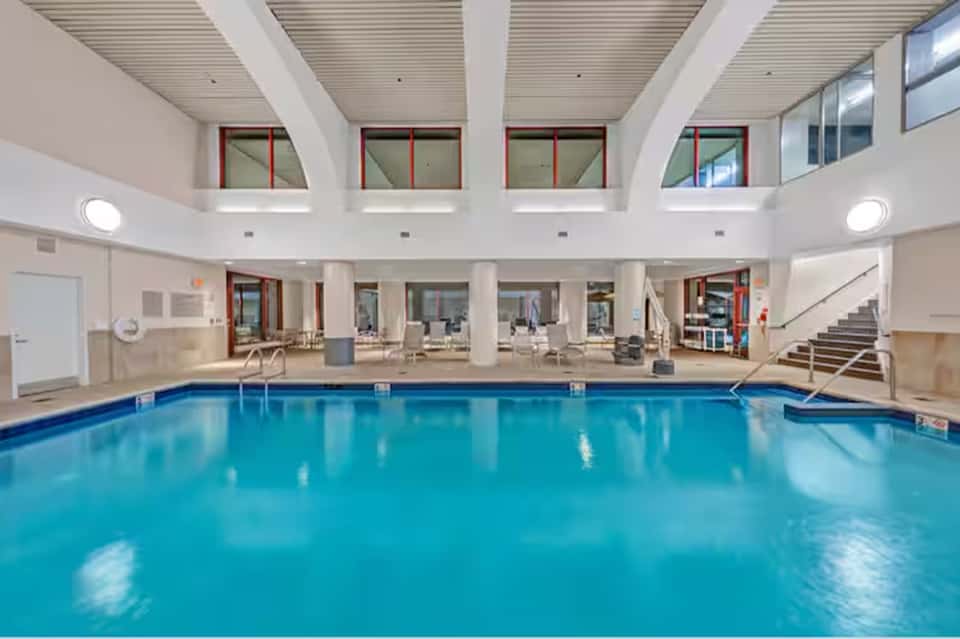 Indoor swimming pool with bright blue water, skylights, and surrounding seating areas in a spacious facility
