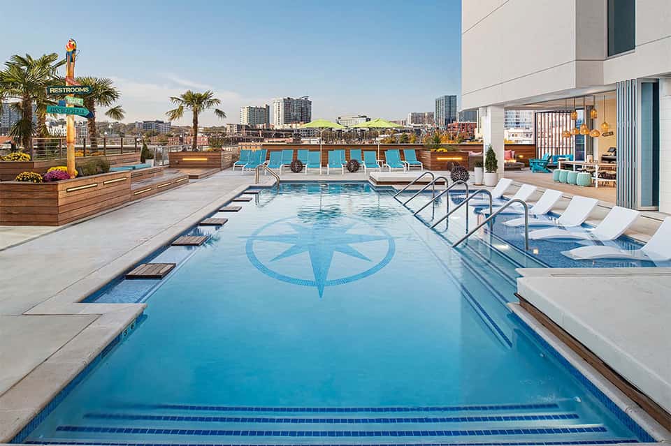 Rooftop swimming pool with compass design, blue lounge chairs, and city skyline view