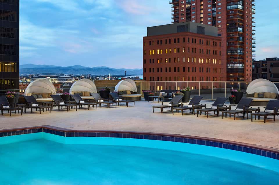 Rooftop pool with lounge chairs and dome cabanas overlooking city skyline at dusk