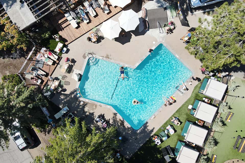Aerial view of resort pool surrounded by lounge chairs, umbrellas, and landscaping with wooden deck