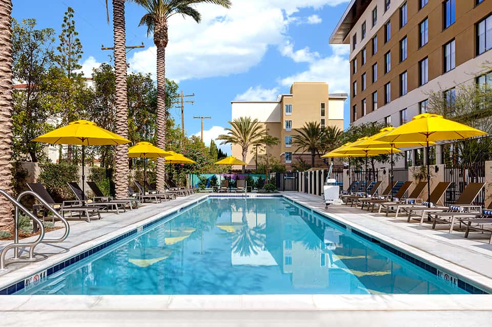 Resort pool with bright yellow umbrellas, palm trees, and modern apartment buildings