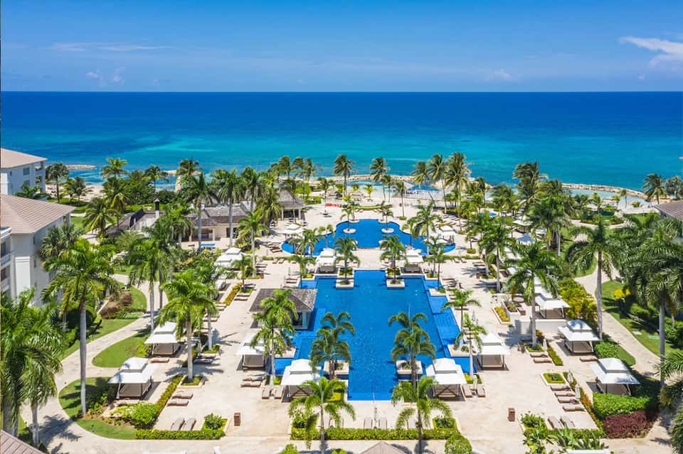 Aerial view of large resort with multiple pools, palm trees, and beachfront property along turquoise ocean