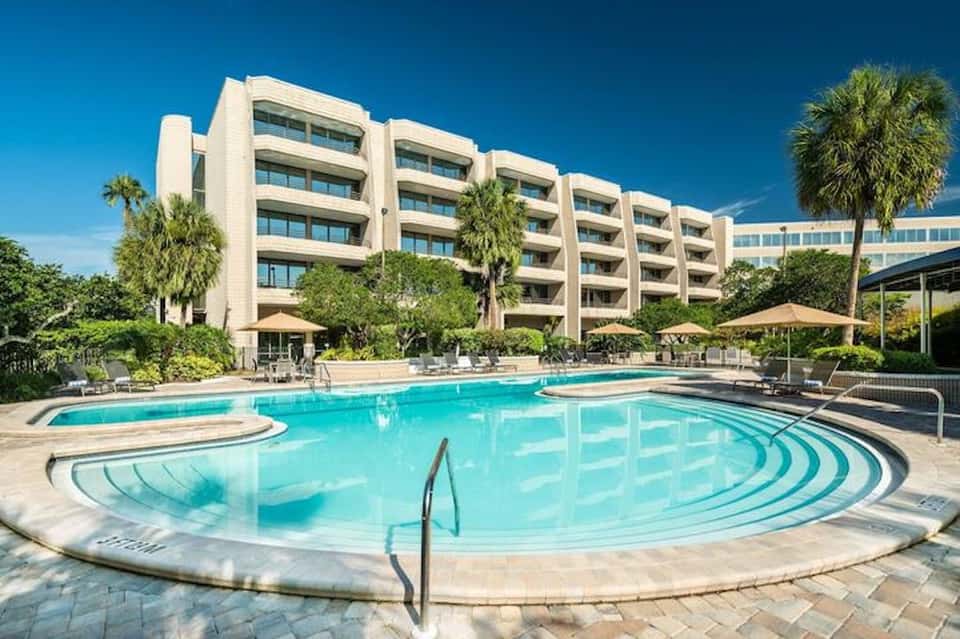Resort pool complex with curved lap lanes, white building, and palm tree landscaping