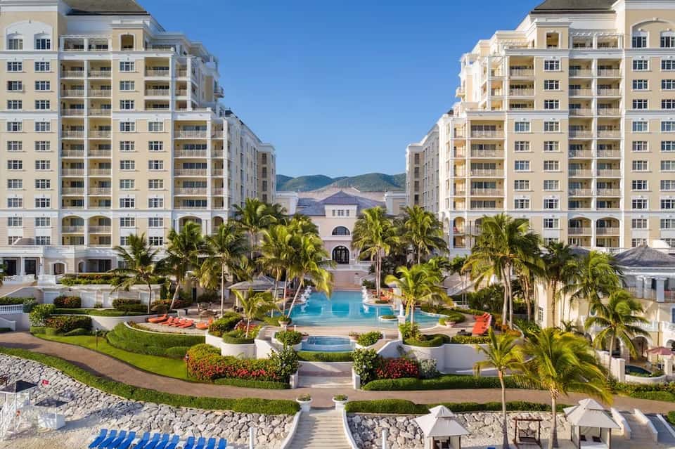 Resort courtyard with pool, palm trees, surrounding apartment buildings, and mountain backdrop