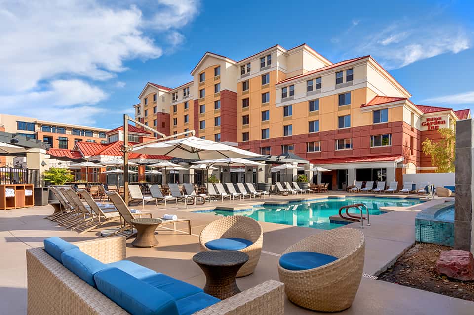 Resort outdoor pool area with lounge chairs, umbrellas, and multi-story hotel building with orange/red accents