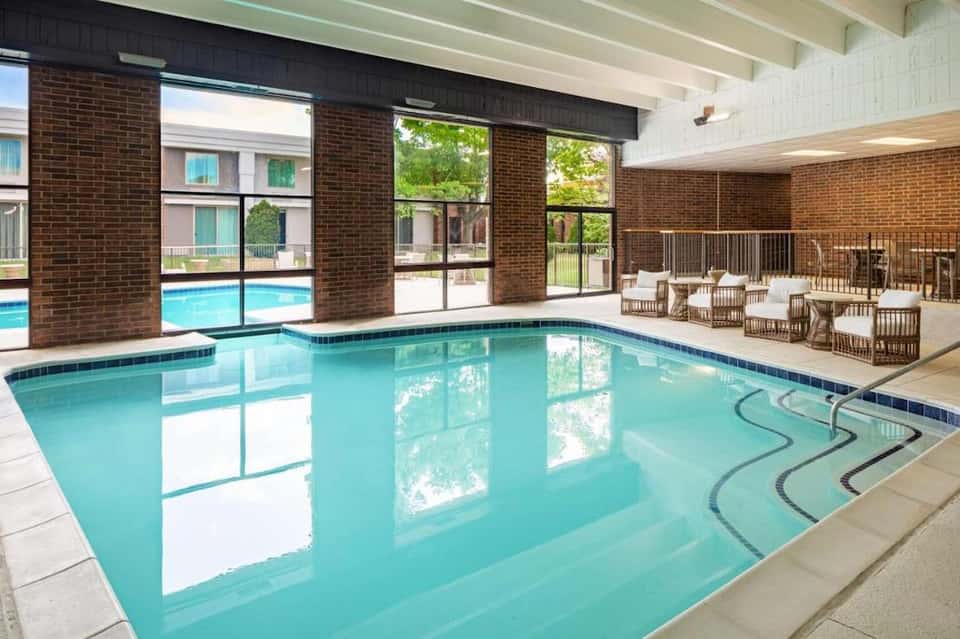Indoor swimming pool with turquoise water, brick walls, large windows, and lounge seating area