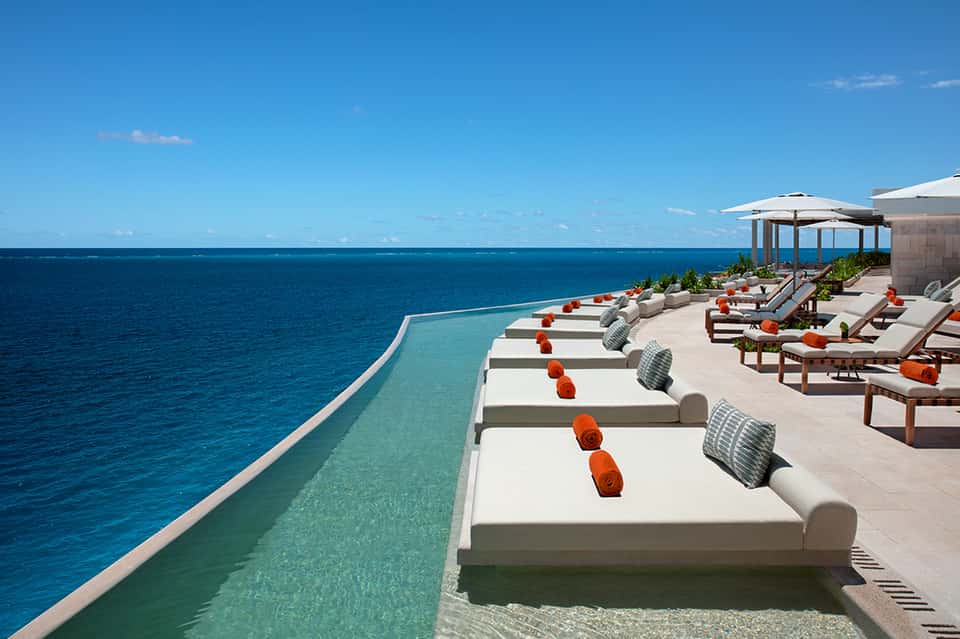 Infinity pool overlooking the ocean with white loungers, umbrellas, and turquoise water