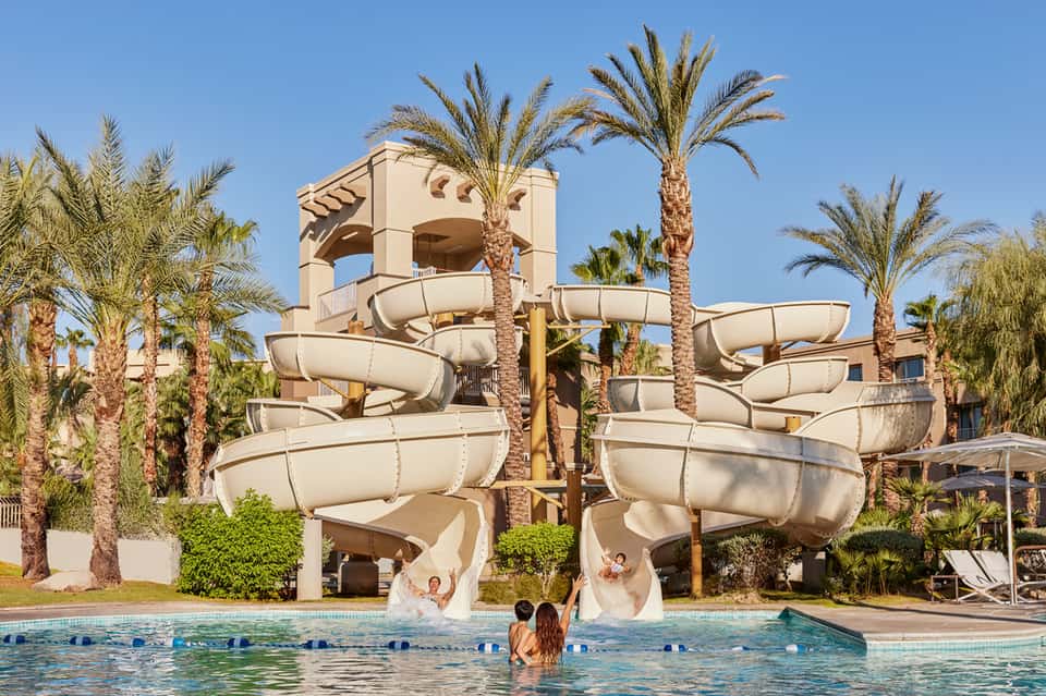 Family water park with large spiral water slides, palm trees, and guests in turquoise pool