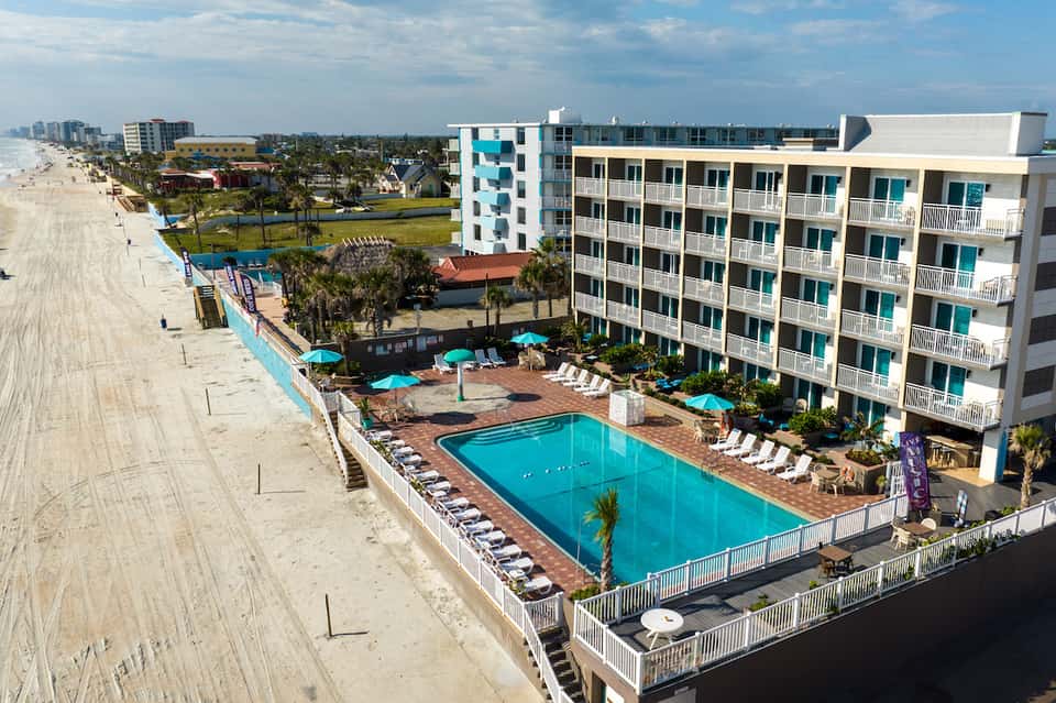 Beachfront resort with bright turquoise pool, multi-story building, umbrellas, and sandy beach