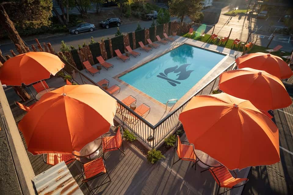Resort pool deck with red umbrellas, loungers, and surrounding hedges