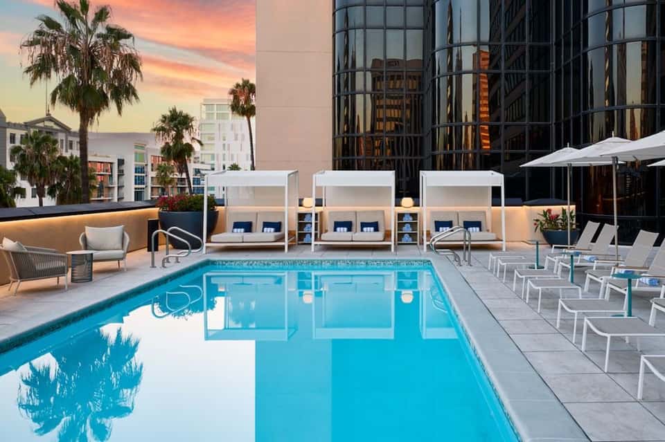 Modern rooftop pool at sunset with white cabanas, lounge chairs, and downtown city skyline views