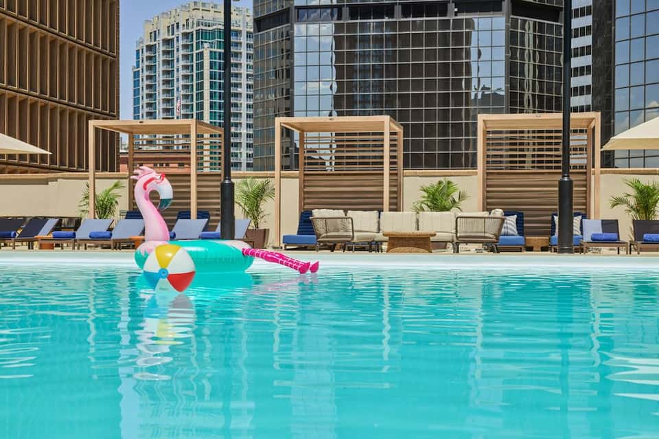Vibrant turquoise rooftop pool with inflatable flamingo float and colorful beach ball, city skyline views