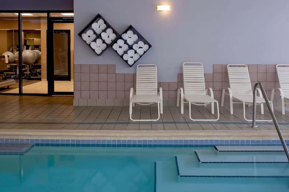 Indoor pool area with white lounge chairs and decorative towel wall art display