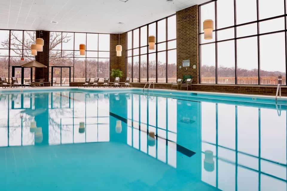 Indoor lap pool with large windows, wooden beams, and lounge chairs in a modern facility