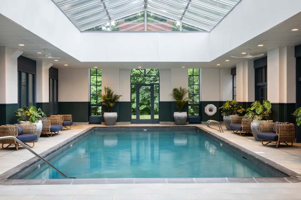 Indoor pool with skylight ceiling, wicker lounge chairs, green accent walls, and large windows