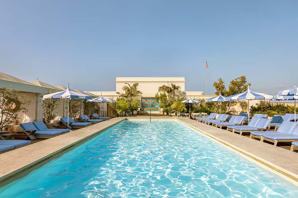 Resort rectangular pool with turquoise water, white umbrellas, and blue loungers on surrounding deck