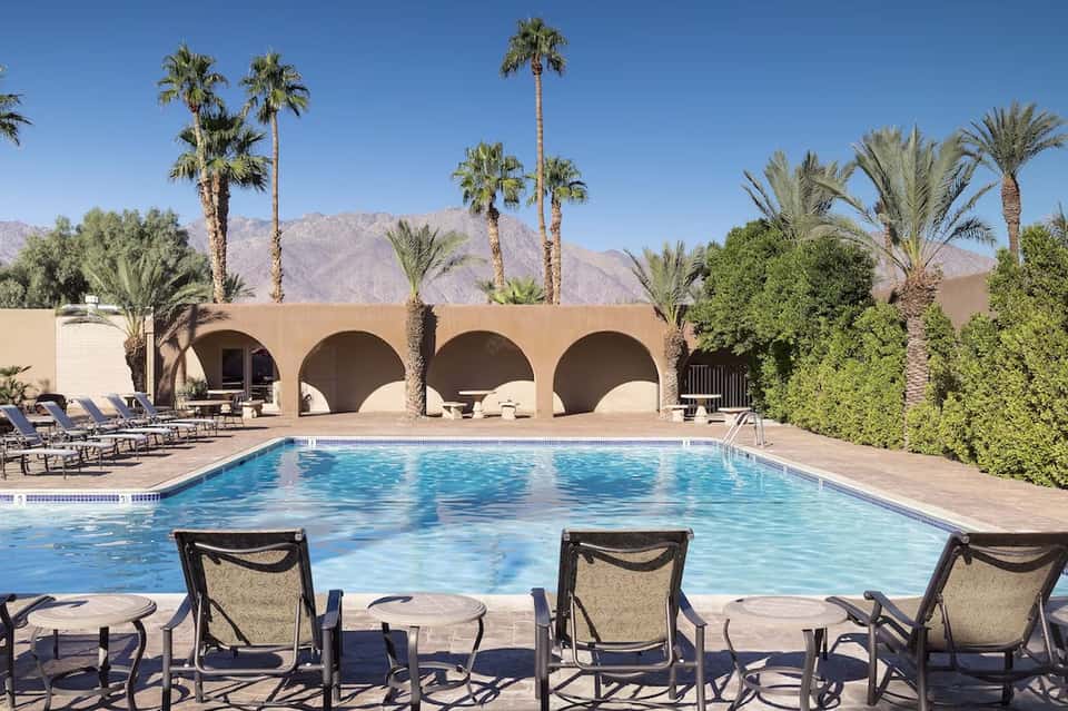 Desert resort pool with arched architectural features, lounging area, and mountain backdrop