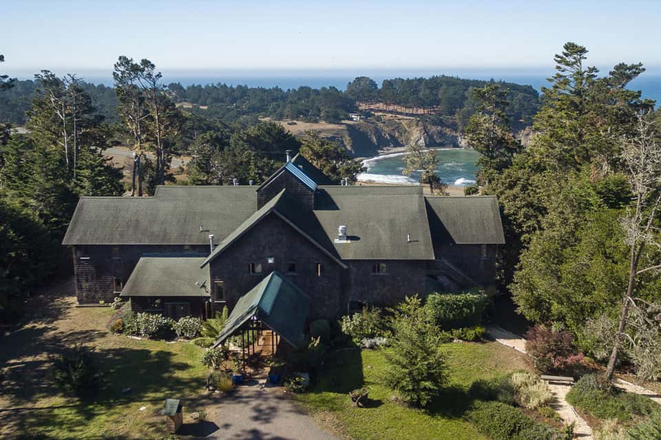 Modern dark house with multiple roof peaks overlooking coastal cliffs and ocean