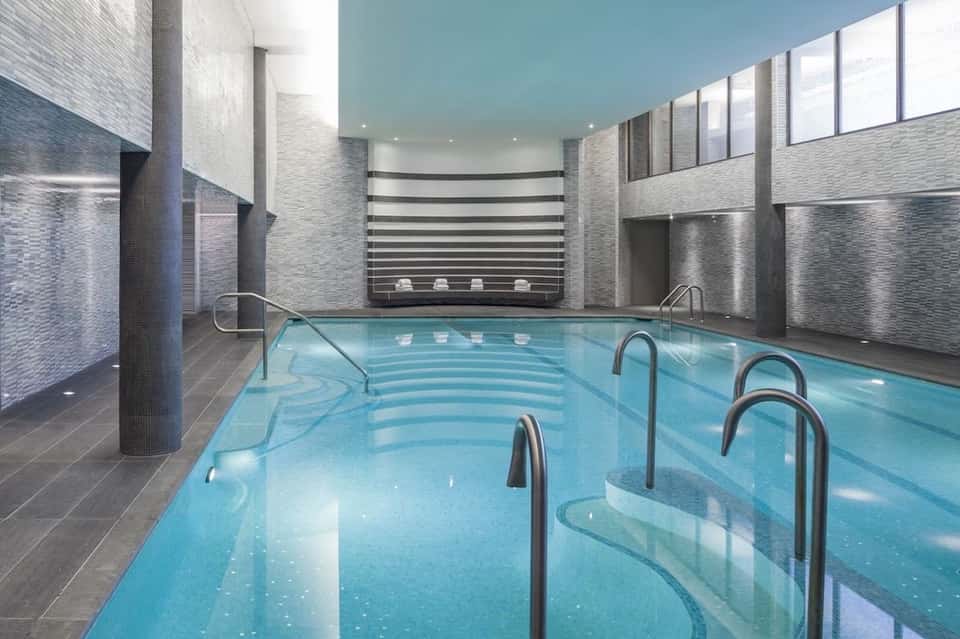 Indoor lap pool with modern gray brick walls, skylights, and seating area in contemporary wellness facility