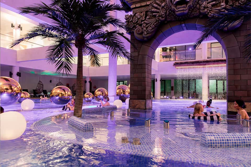 Indoor pool with purple lighting, palm trees, golden spheres, and modern architectural arches