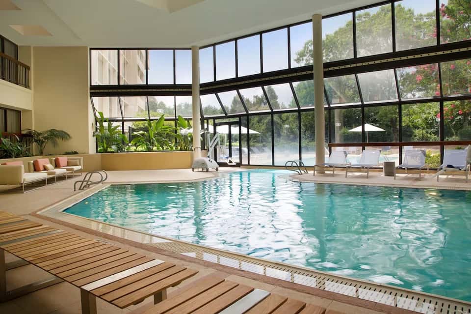 Indoor pool with large windows overlooking gardens, wooden deck, lounge chairs, and natural lighting