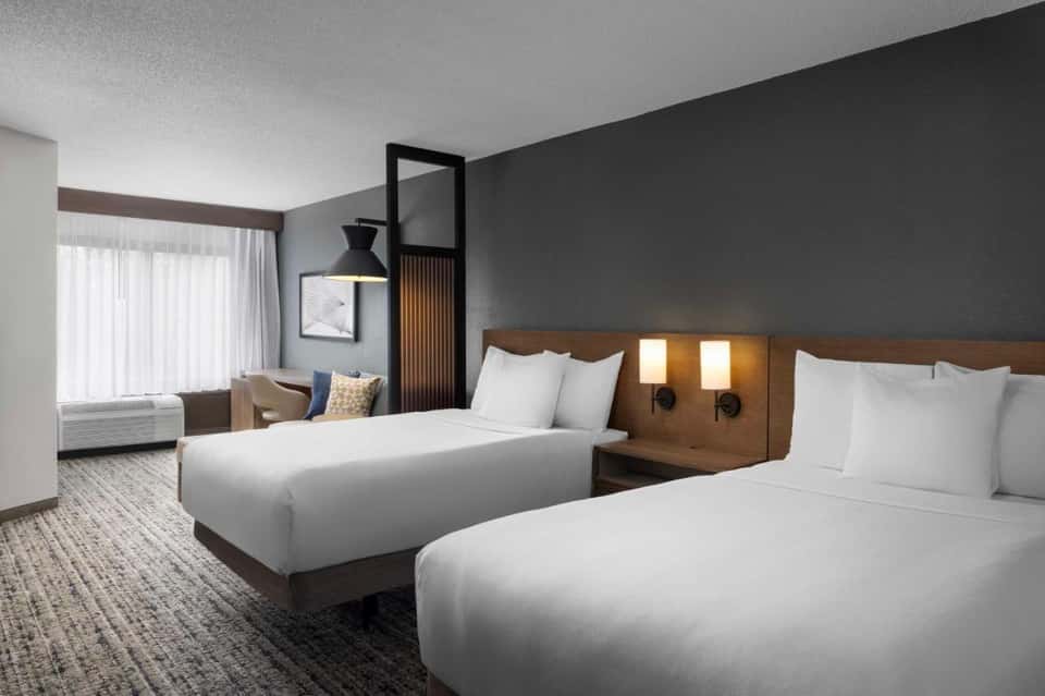 Hotel bedroom with two queen beds, gray walls, wooden headboard, and seating area