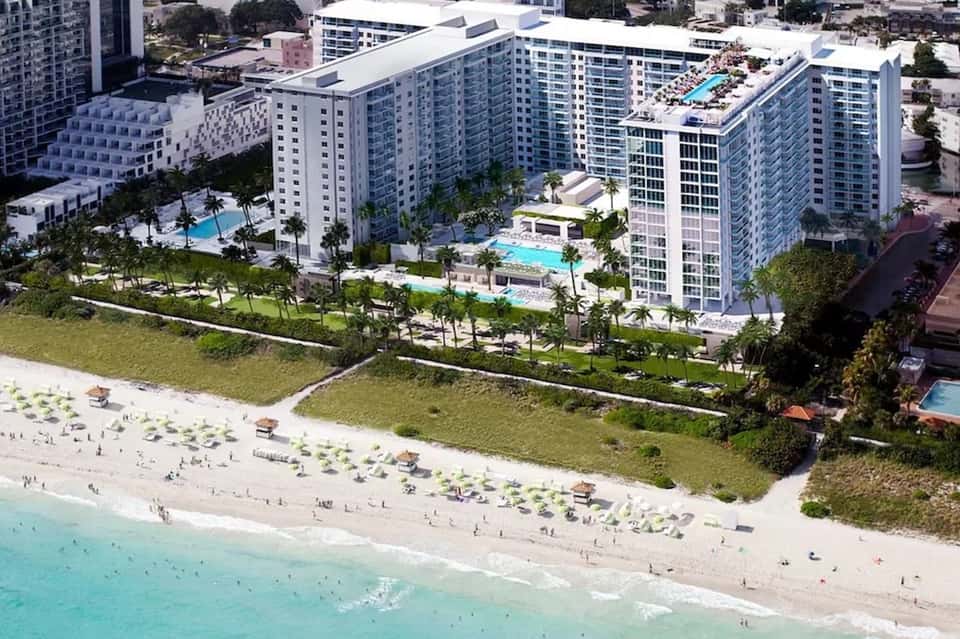 Aerial view of beachfront resort with multiple high-rise towers, pools, and sandy beach