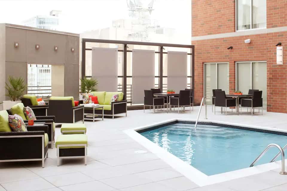 Modern rooftop pool with lime green loungers, black frames, heating elements, and city skyline