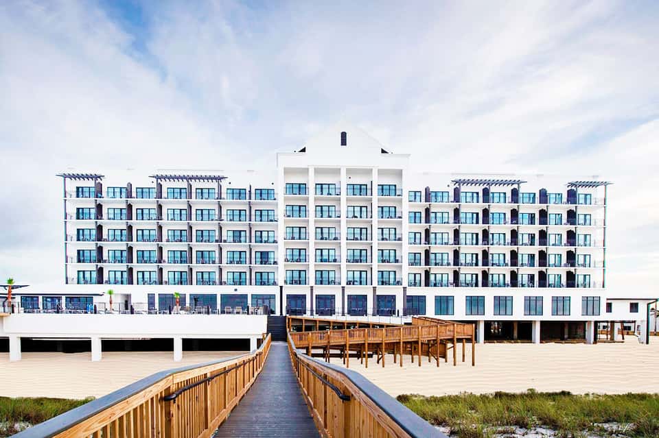 Modern beachfront hotel with white and blue facade, wooden boardwalk leading to sandy beach