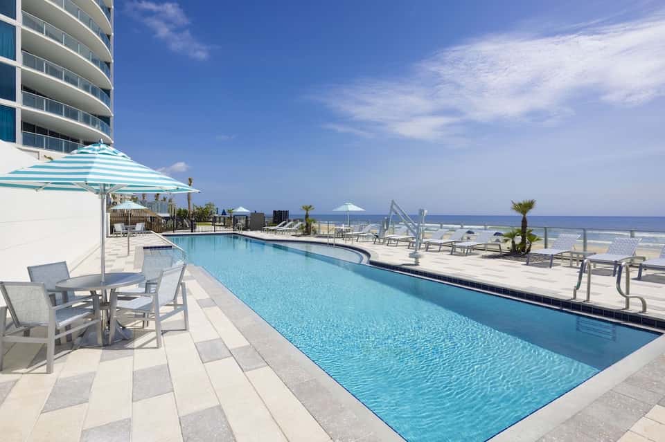 Beachfront resort pool with lounge chairs, striped umbrella, and ocean view
