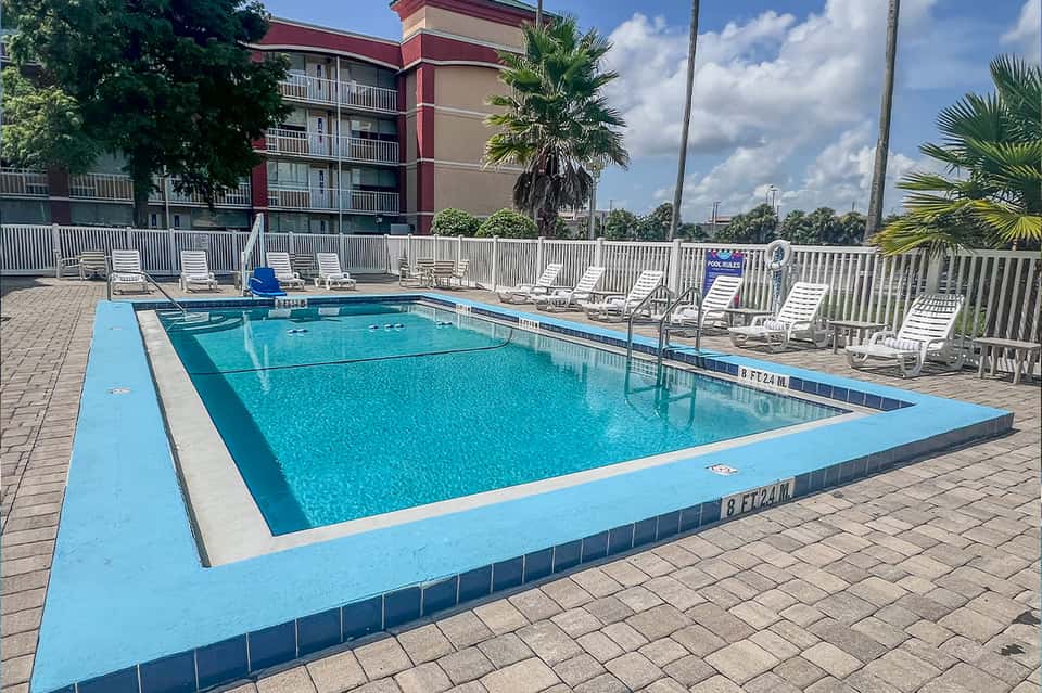 Rectangular resort pool surrounded by white lounge chairs and palm trees